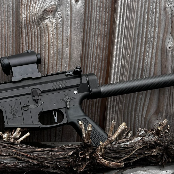 Black tactical rifle with scope and suppressor resting on twisted wood against weathered wooden background