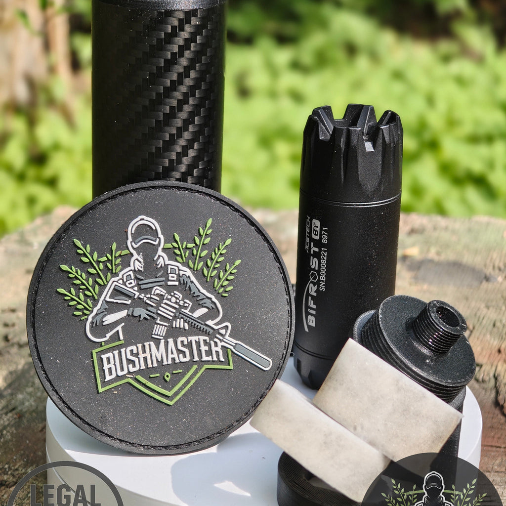 Bushmaster patch with soldier holding rifle, black firearm parts, and carbon fiber tube on wooden surface