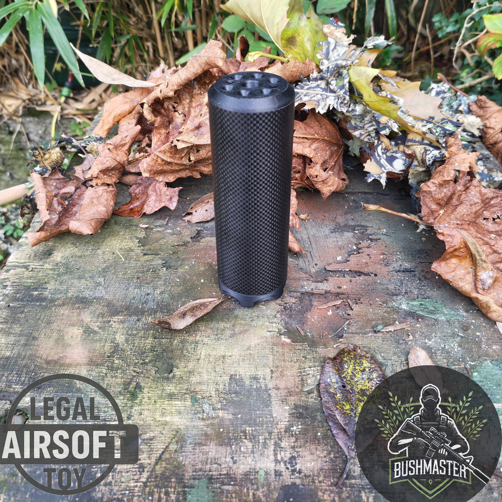 Black airsoft suppressor on weathered wooden surface with dry leaves, Bushmaster logo