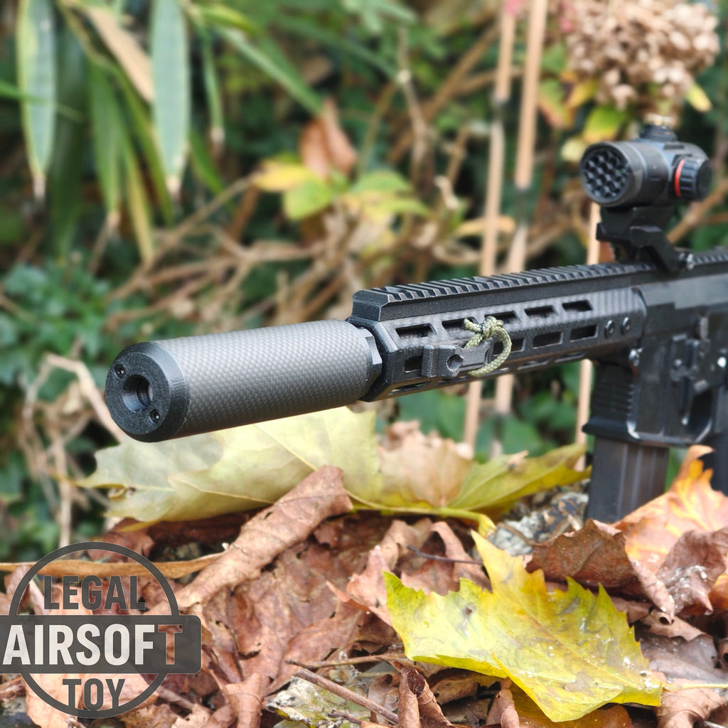 Black airsoft rifle with suppressor and red dot sight resting on autumn leaves outdoors