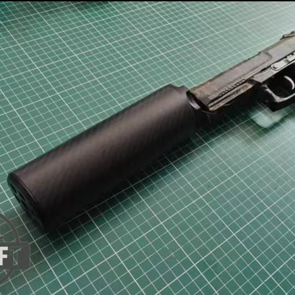 Black tactical handgun with attached cylindrical suppressor on green cutting mat surface