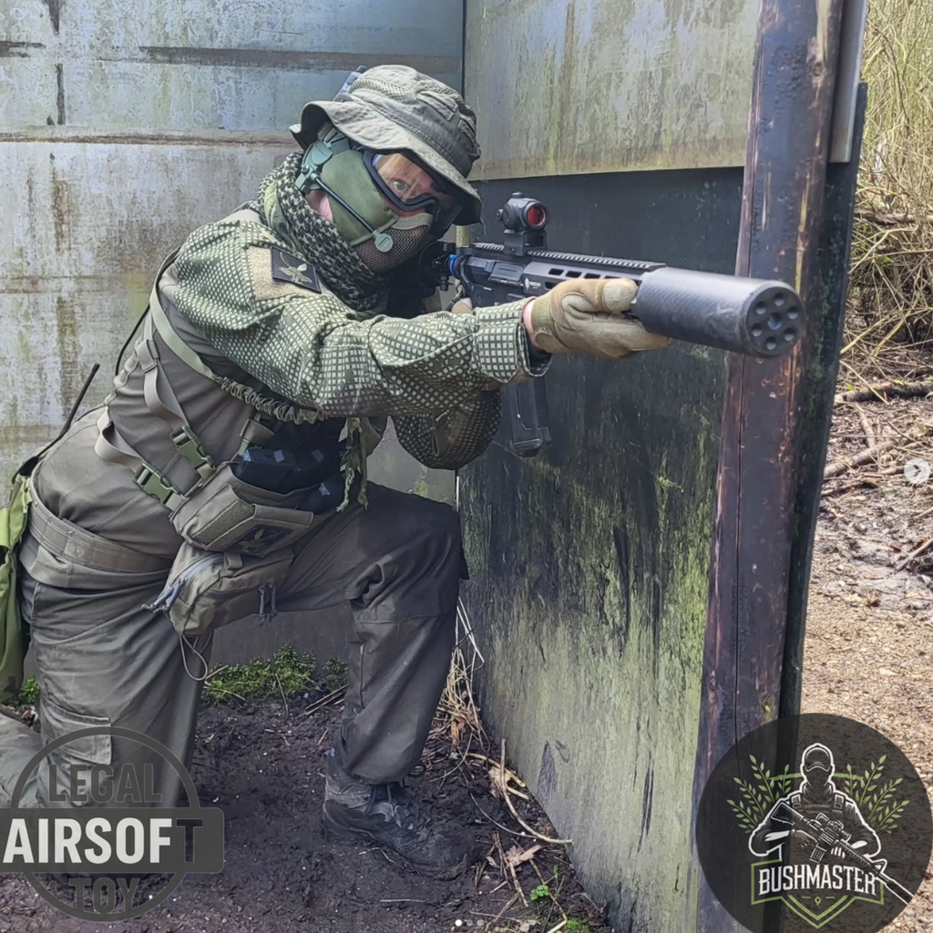 Camouflaged airsoft player aiming rifle with silencer behind weathered barrier outdoors