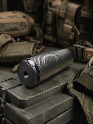 Bushmaster Big Boy Gen 3 carbon-fiber sound moderator lying on tactical cases with the threaded rear cap visible