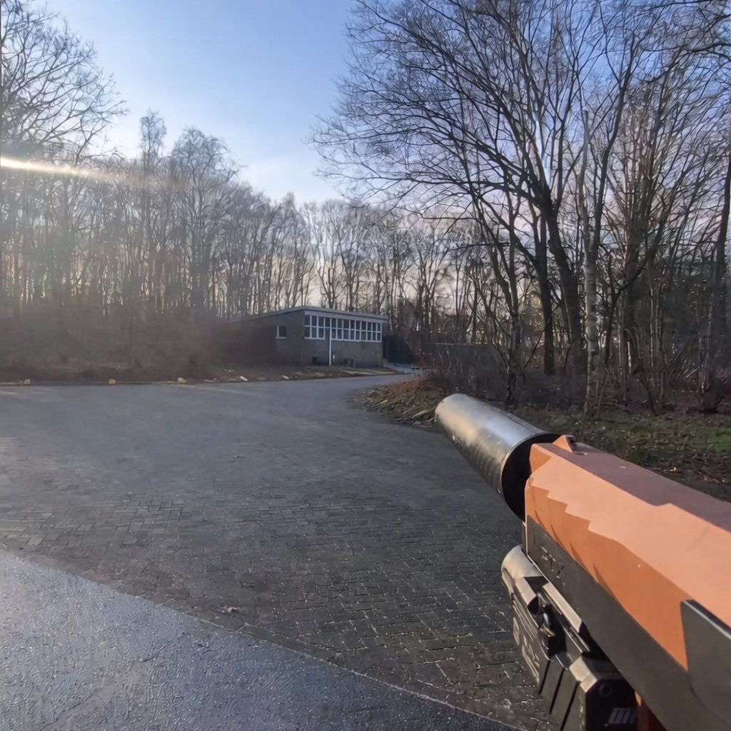 First-person view of an airsoft gun with suppressor in a quiet outdoor wooded area near a paved road and building