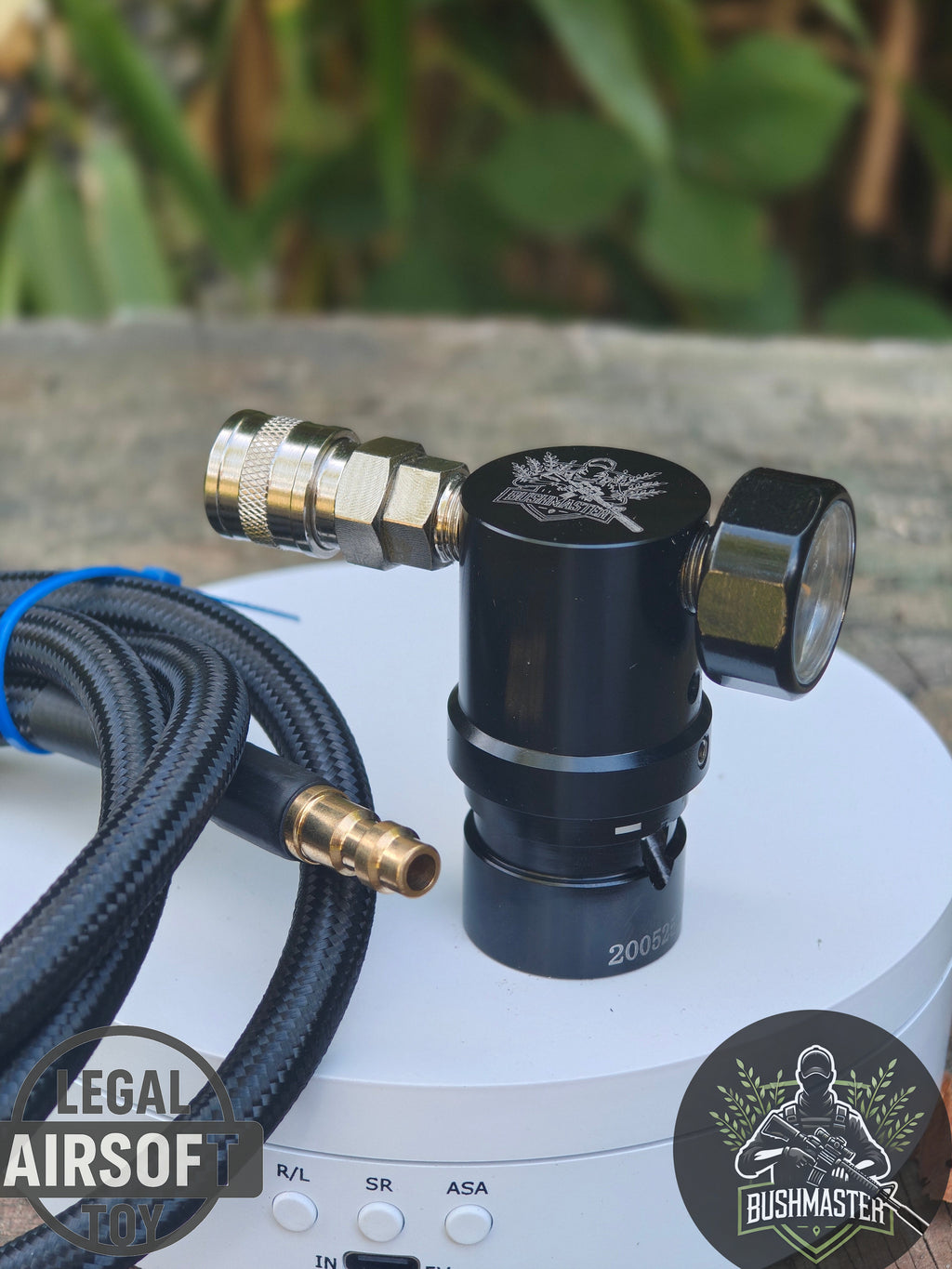 Bushmaster branded black airsoft CO2 regulator with pressure gauge and braided hose on white surface