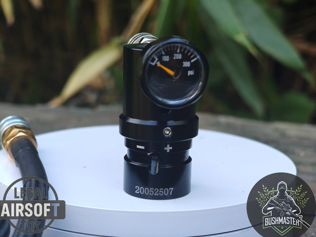 Black airsoft pressure regulator with gauge on white surface, outdoor setting with green foliage