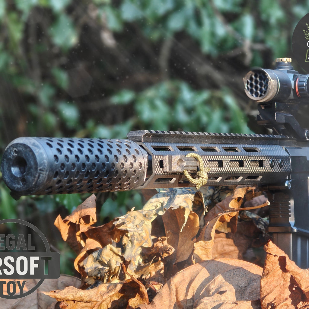 Close-up of a black airsoft rifle with a suppressor and scope resting on dry leaves outdoors